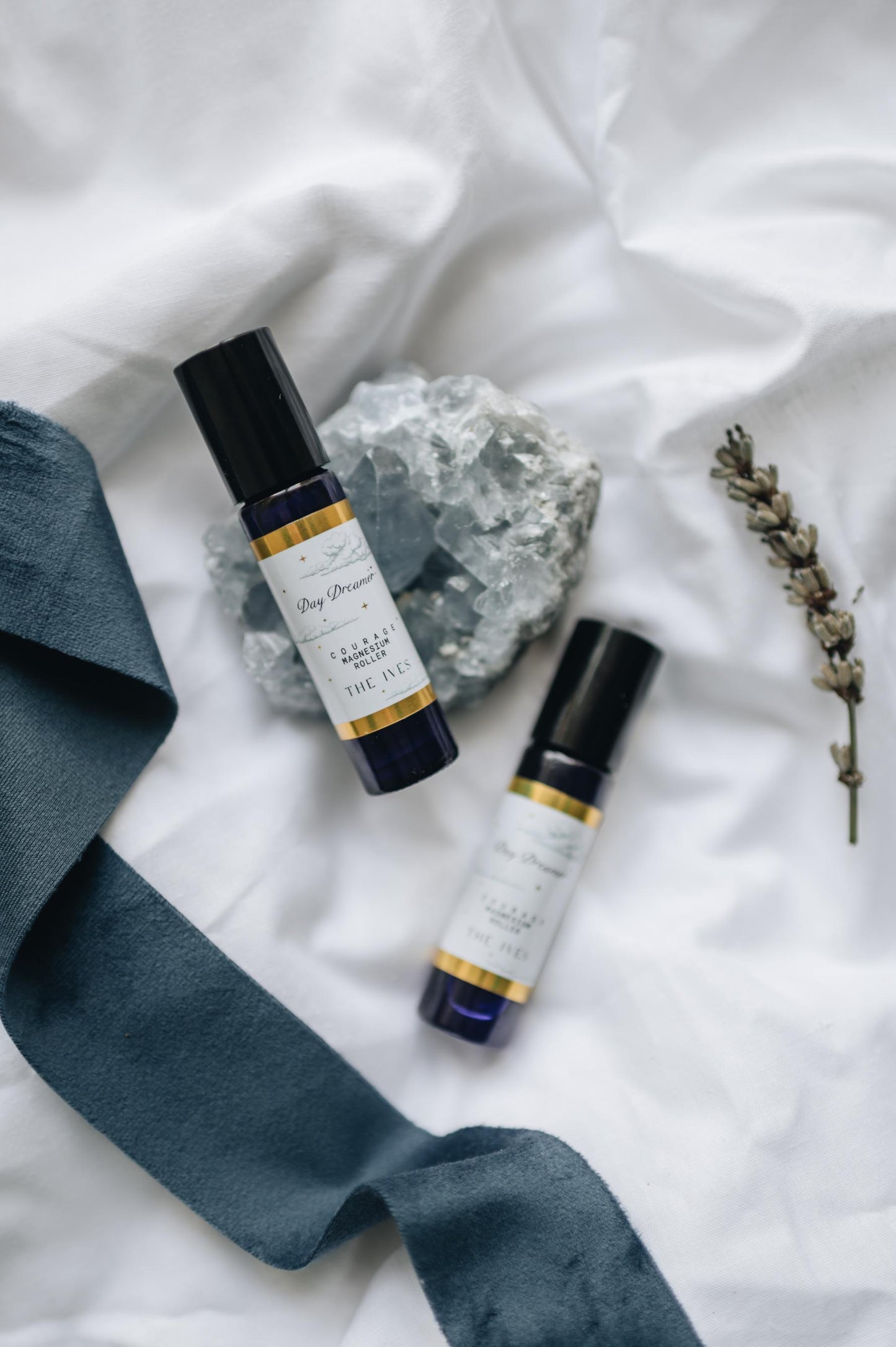 magnesium oil anxiety relief essential oil roller lying on crystal with lavender and white linin background. Blue glass roller for when anxiety strikes and courage is needed. handmade, vegan, natural ingredients.