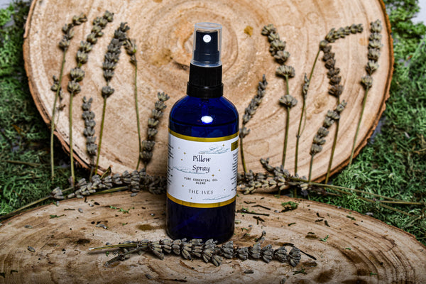 Sleep spray in blue glass bottle in front of a wooden tree ring and fresh lavender and moss natural vegan and handmade pillow spray